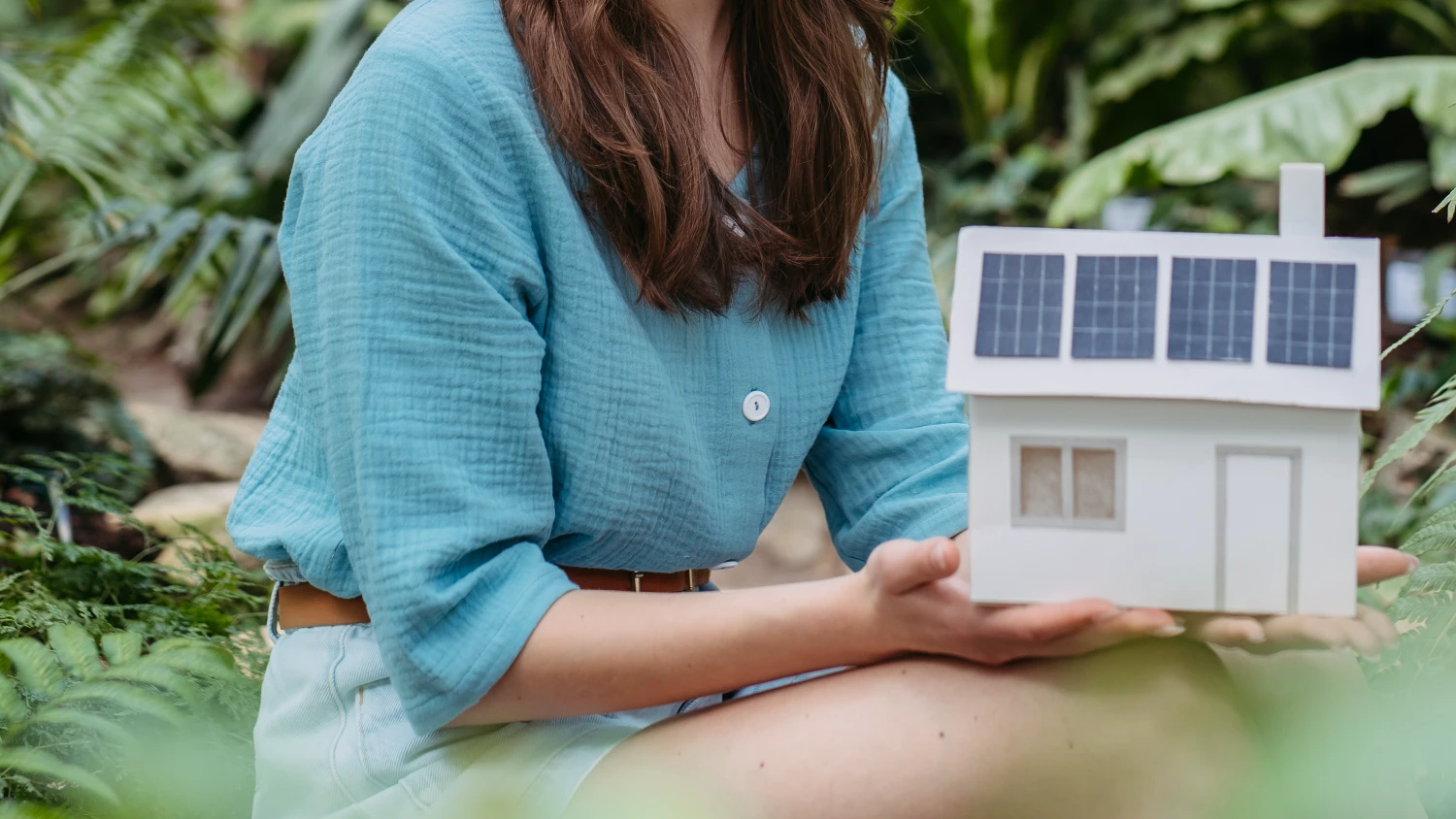 Frau hält Miniaturhaus mit Solarpanelen
