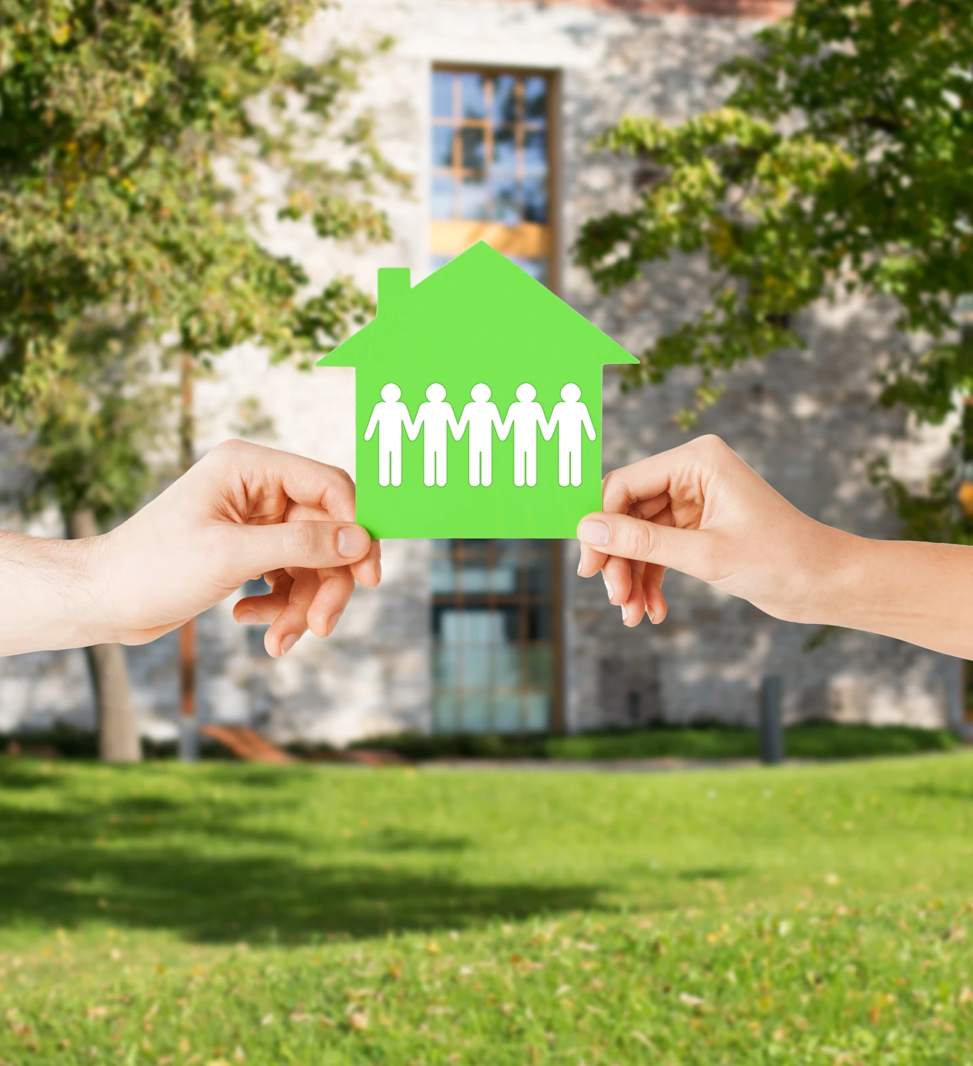 Zwei Hände halten grünes Haus mit Menschenfiguren
