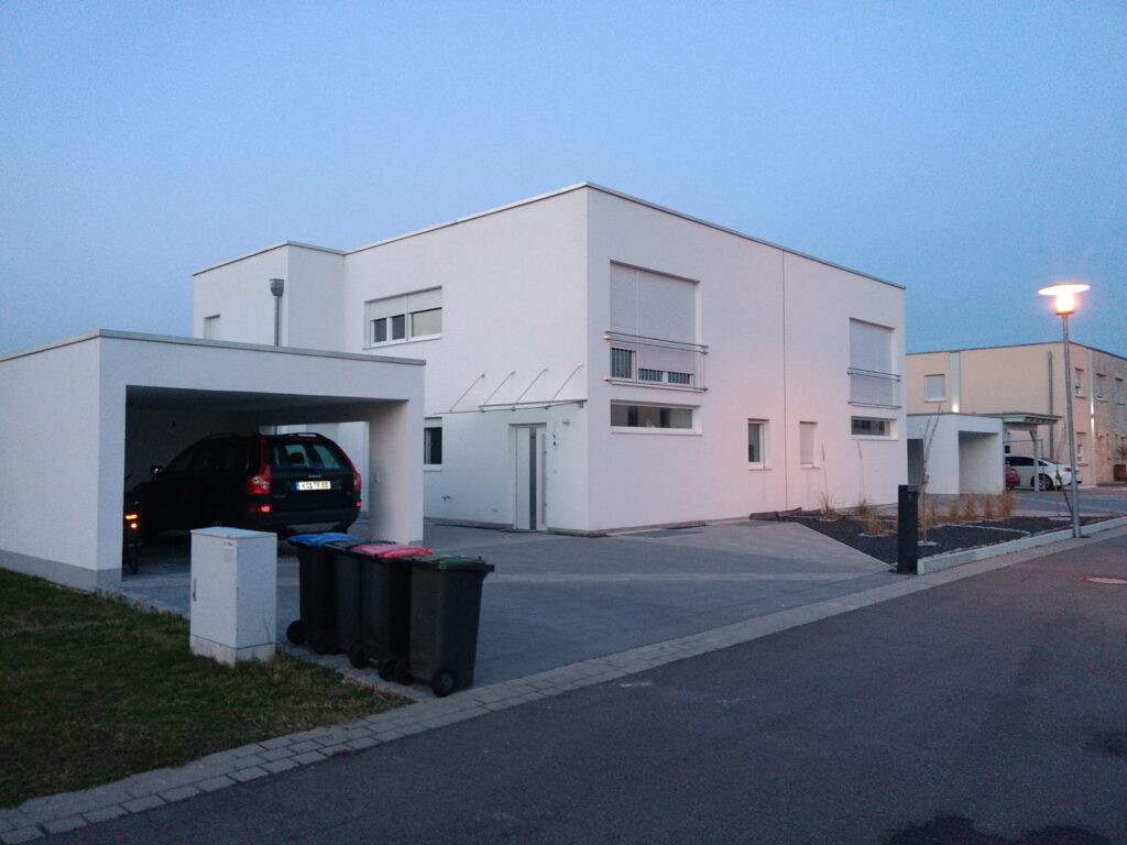 Modernes weißes Einfamilienhaus mit Carport bei Abenddämmerung